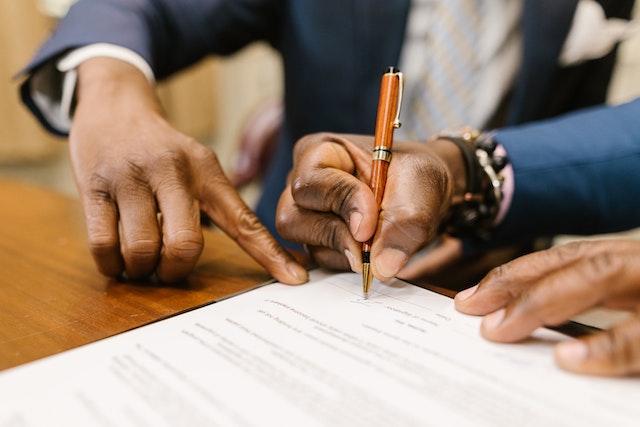 one person signing a contract as someone else points to the signature line